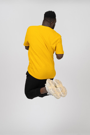 Back view of a jumping young dark-skinned man in yellow t-shirt