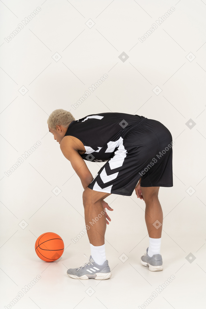 Vista posterior de tres cuartos de un joven jugador de baloncesto masculino de pie junto a la pelota
