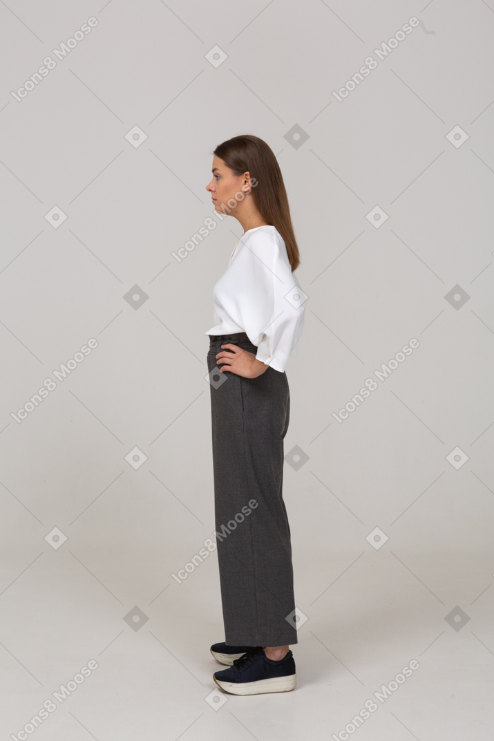Вид сбоку серьезной молодой леди в офисной одежде, положившей руки на бедра