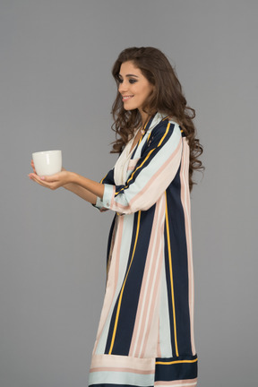 Gaie jeune femme arabe tenant une tasse blanche avec les deux mains
