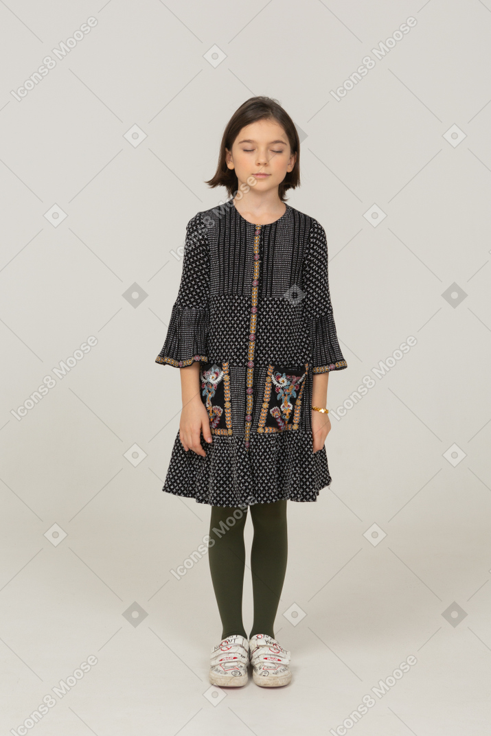 Vista frontal de una niña en vestido de pie con los ojos cerrados.