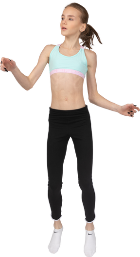 Vista frontal de uma adolescente em roupas esportivas levantando as mãos e olhando para o lado enquanto pula