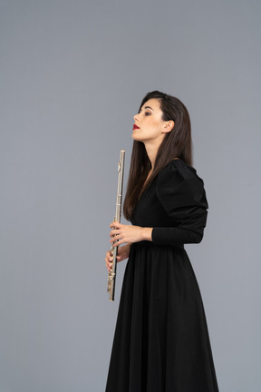 Side view of a serious young lady in black dress holding flute