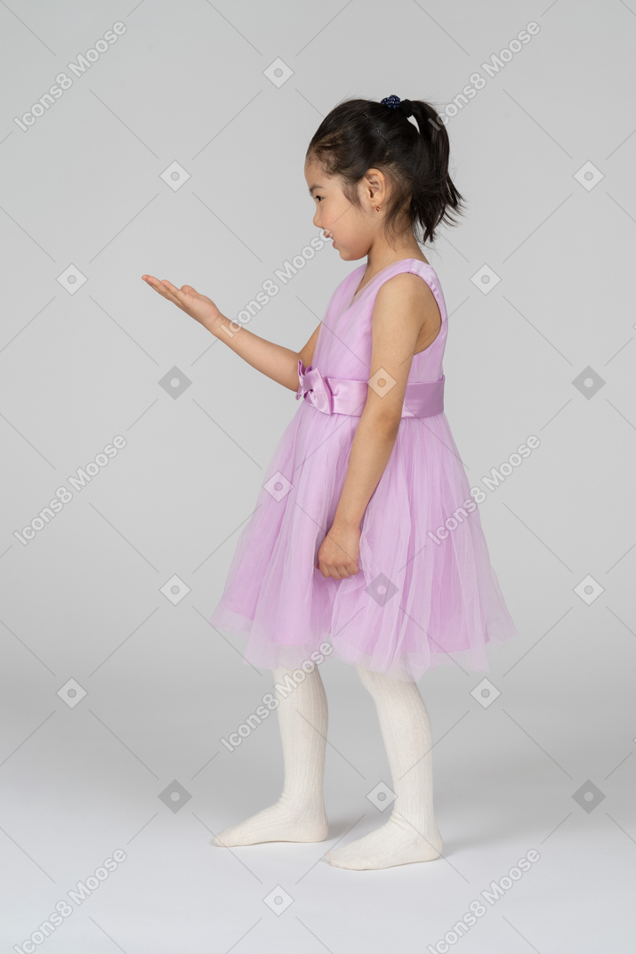 Side view of a little girl in a tutu dress raising her arm while talking