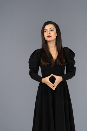 Front view of a bossy young lady in a black dress holding hands together