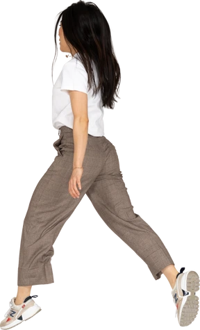 Three-quarter back view of a jumping young lady in breeches and t-shirt outspreading her legs