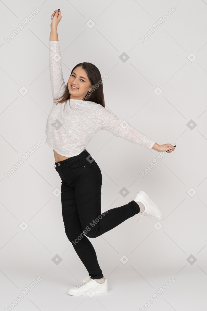 Side view of a smiling young dancing indian female in casual clothes raising hand