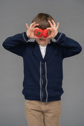 Portrait of a little boy hiding his eyes behind two tomatoes