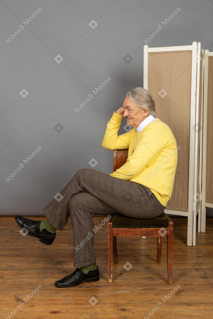 Мужчина сидит на стуле и подпирает голову рукой