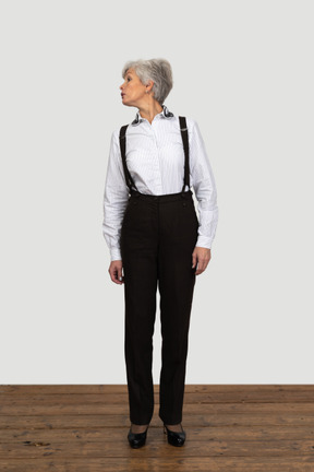 Front view of an old female in office clothes standing still indoors looking aside