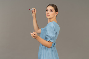 Vista lateral, de, un, mujer joven, en, vestido azul, tenencia, un, lápiz labial
