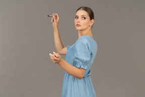 Side view of a young woman in blue dress holding a lipstick