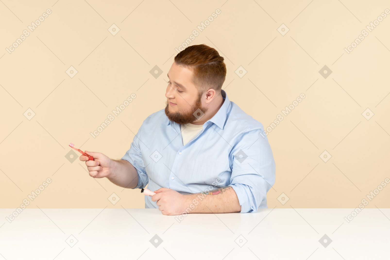 Большой человек сидит за столом и держит зубную пасту и зубную щетку