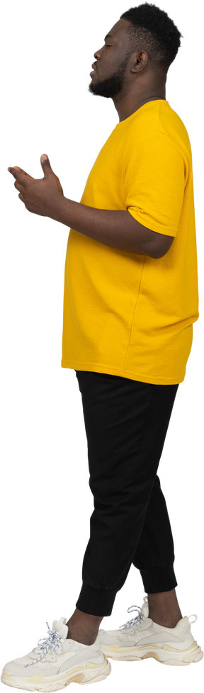 Vista lateral de un joven hombre de piel oscura gesticulando pensativo en camiseta amarilla