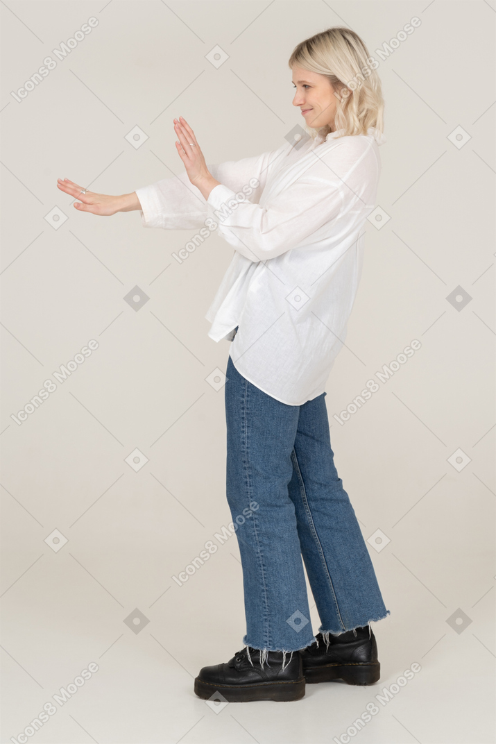 Vista lateral de una mujer rubia estirando los brazos y haciendo muecas