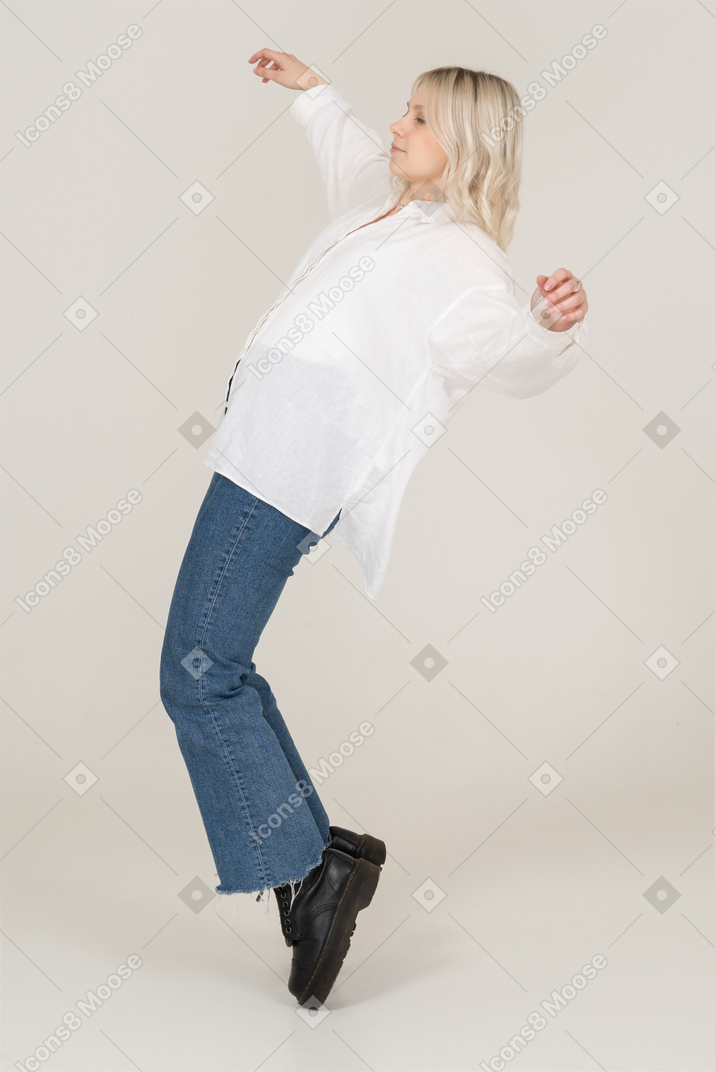 Vista laterale di una donna bionda in piedi sulla punta dei piedi e le braccia aperte