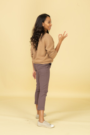 Vista lateral de uma jovem mulher de pele escura mostrando um gesto de ok