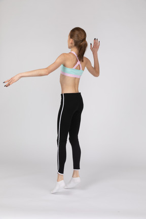 Три четверти сзади девушки-подростка в спортивной одежде, поднимающей руку и прыгающей