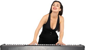 Вид спереди довольной молодой леди в черном платье, играющей на пианино, улыбаясь