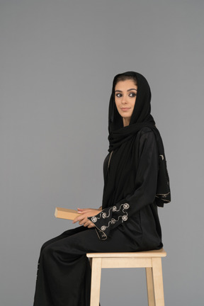 Una mujer árabe cubierta sosteniendo un libro sobre sus rodillas
