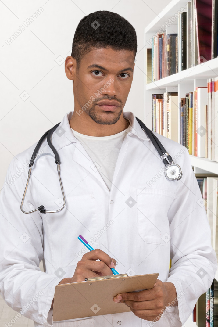 A man in a white lab coat writing on a clipboard