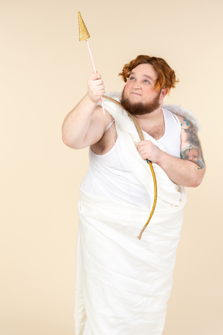 Angry looking big guy dressed as a cupid pointing up with an arrow