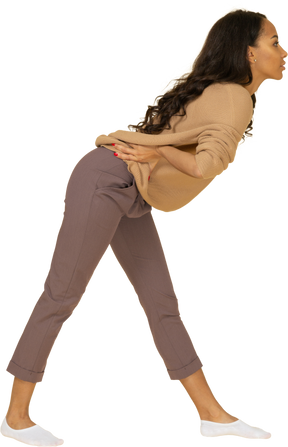 Vista lateral de una mujer joven de piel oscura que pone la mano en la cadera mientras se inclina hacia adelante