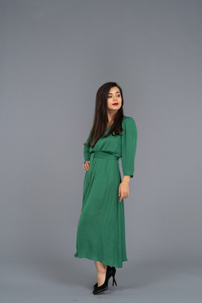Three-quarter view of a young lady in green dress putting hand on hip