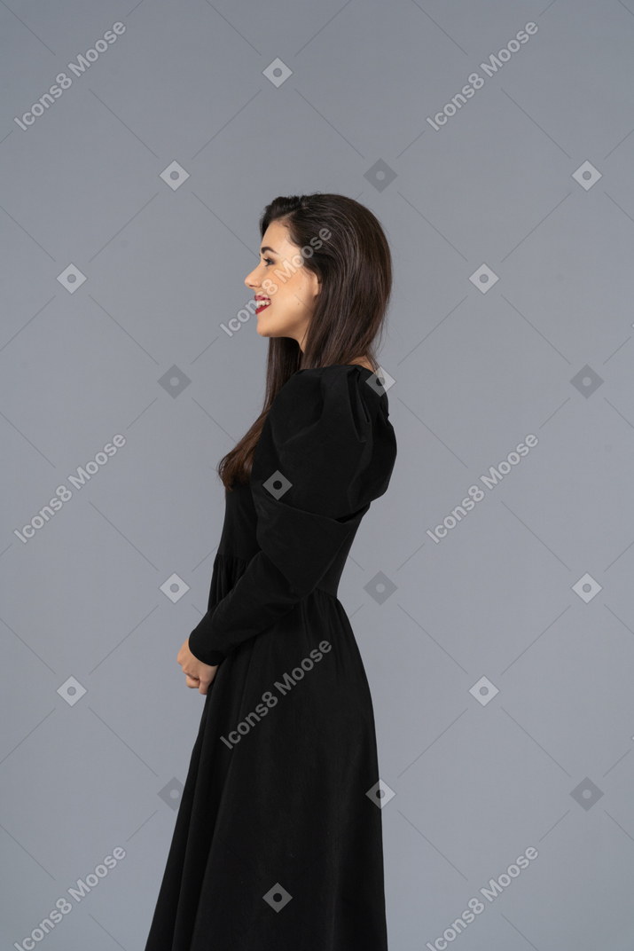 Vista laterale di una giovane donna sorridente in un abito nero in piedi ancora