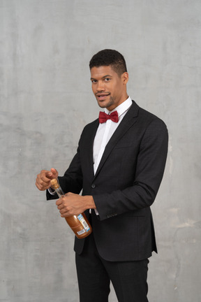 Young man opening a bottle of champagne and looking at camera