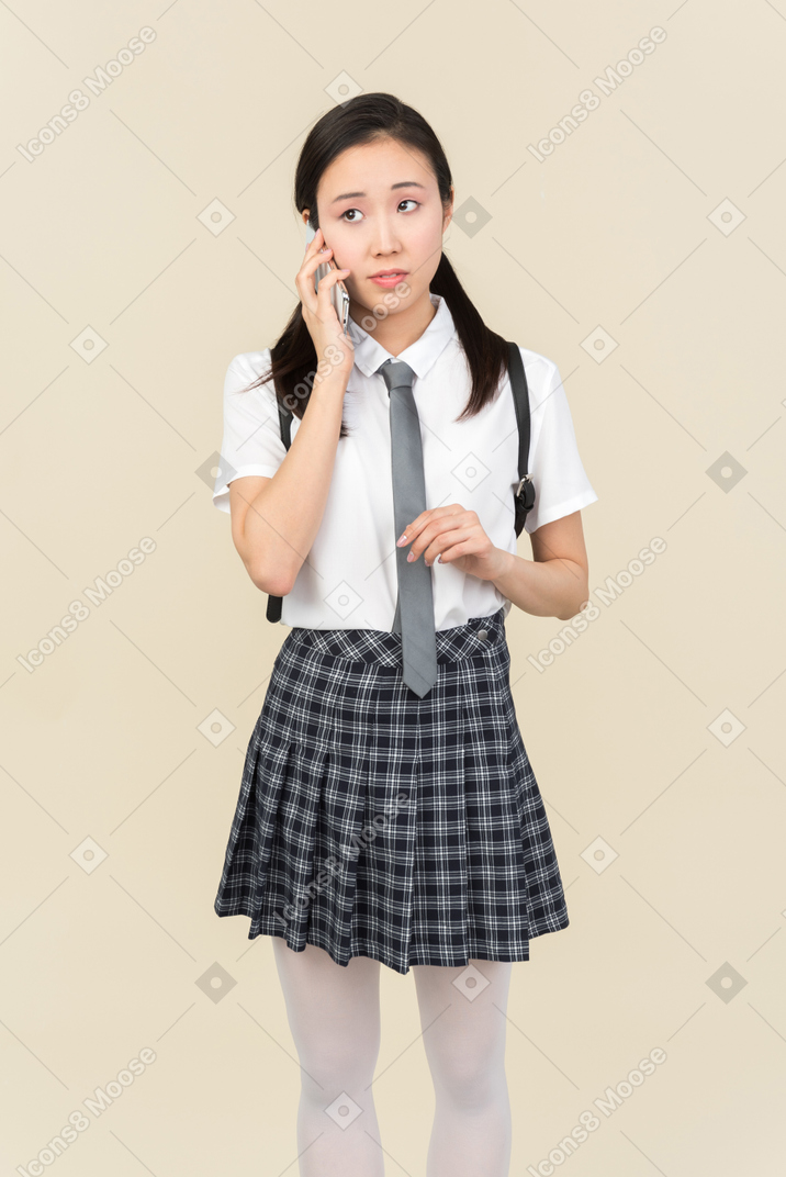 Menina da escola asiática ouvindo atentamente o que é dito no telefone