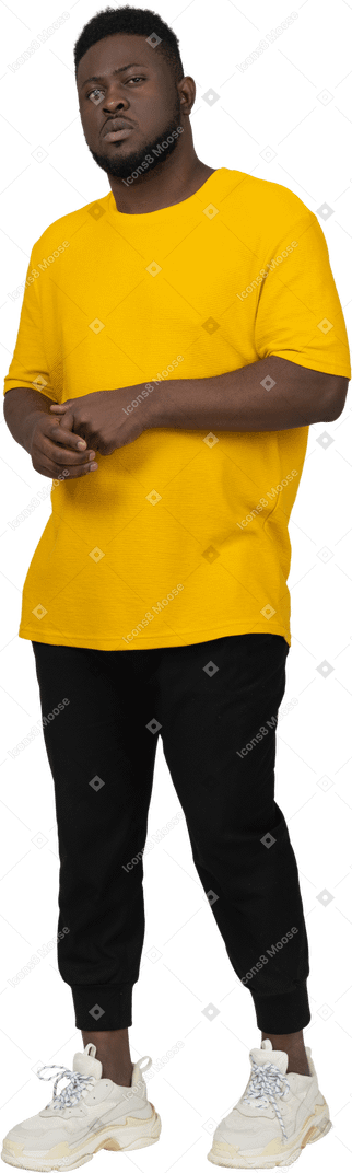 Front view of a young dark-skinned man in yellow t-shirt holding hands together