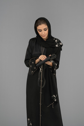 Una donna araba coperta che apre una borsetta nera