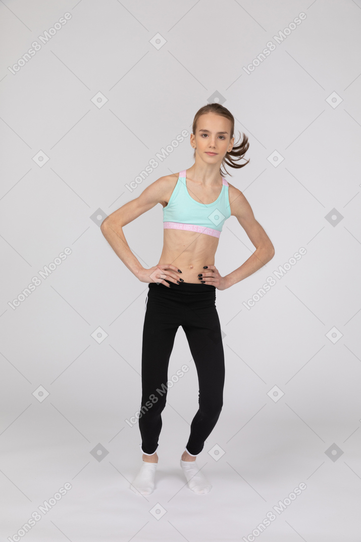 一个年轻的女孩，穿着运动服，将手放在臀部上，弯曲膝盖的前视图