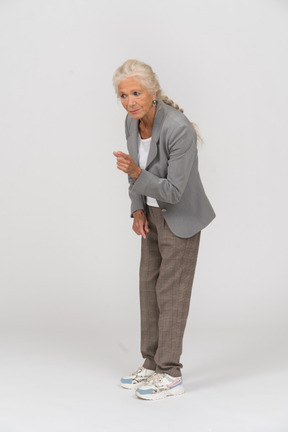 Seitenansicht einer alten dame im anzug, die sich bückt und warnzeichen zeigt
