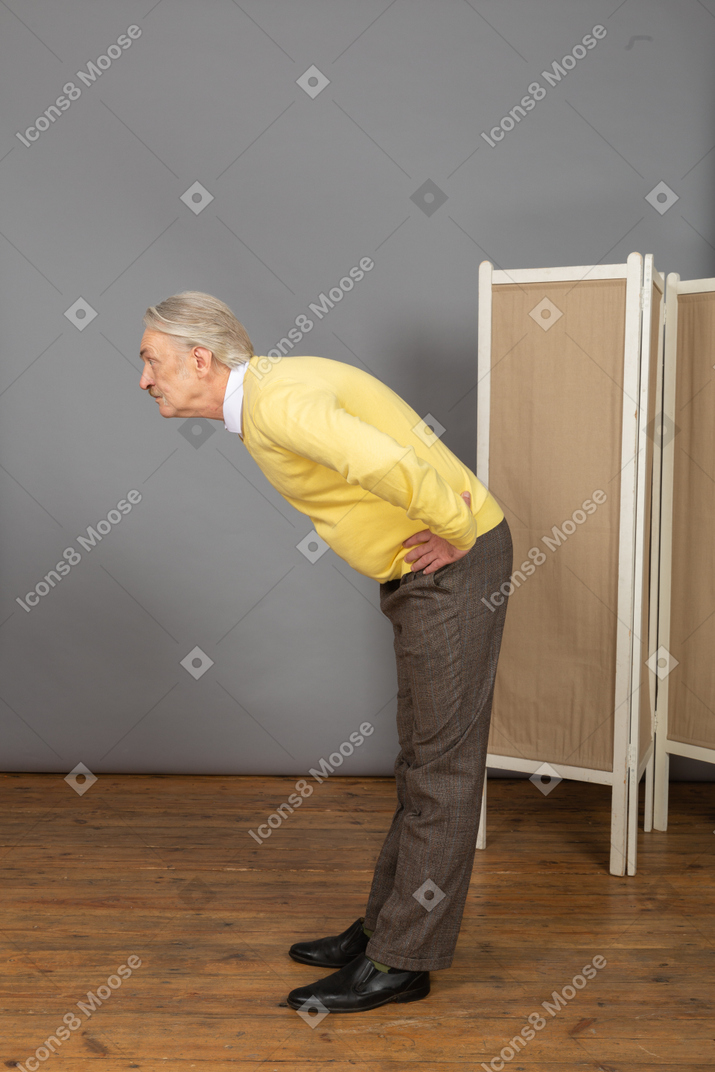 Seitenansicht eines alten mannes, der hände auf hüften legt, während er sich nach vorne beugt