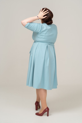 Rear view of a woman in blue dress posing with hand on head