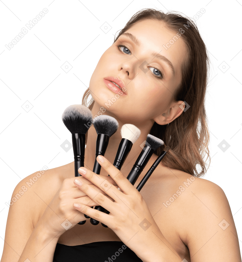 Front view of a sensual young woman holding make-up brushes and tilting head