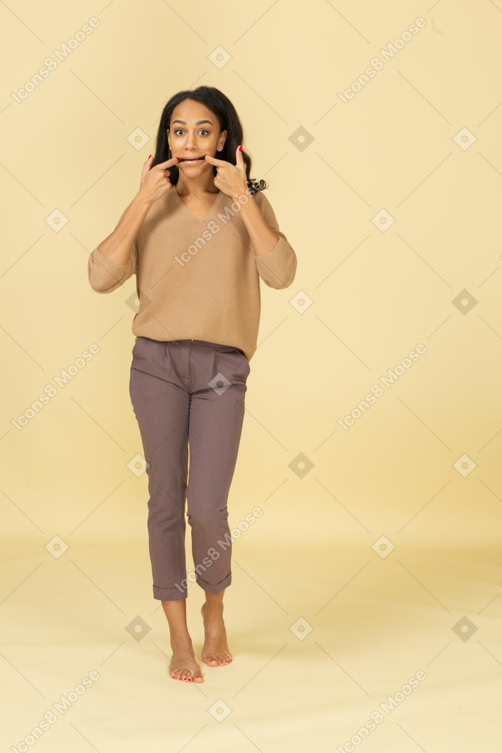 Vista frontal de una joven mujer de piel oscura haciendo muecas tocando su boca