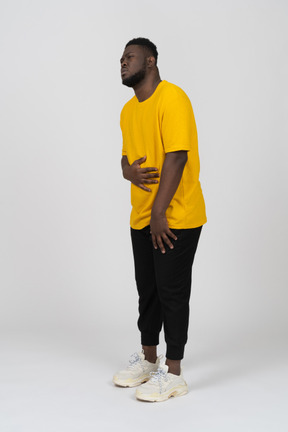 Вид в три четверти молодого темнокожего мужчины в желтой футболке, касающийся живота