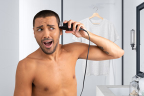 A shirtless man shaving his head in the bathroom