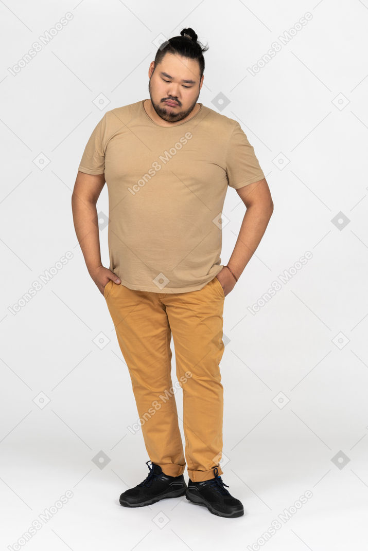 Sad asian man looking down and holding hands in pockets