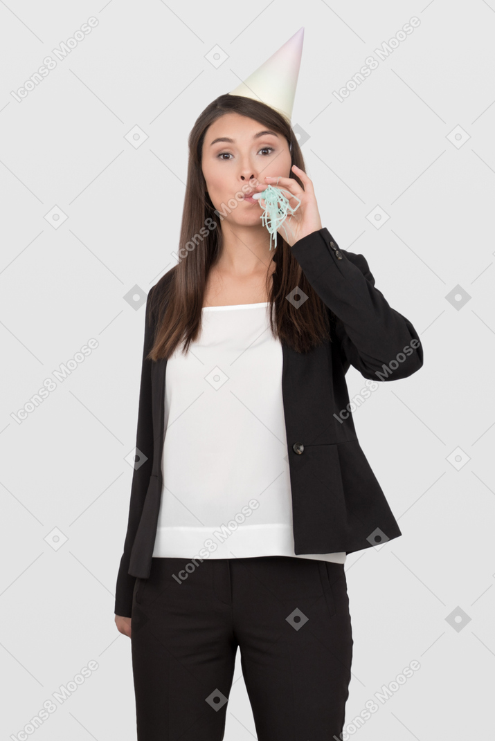 Business woman in a party cap making noise with a blowout whistle