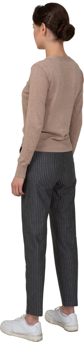 Vista di tre quarti posteriore di una giovane donna in piedi ancora in pullover e pantaloni