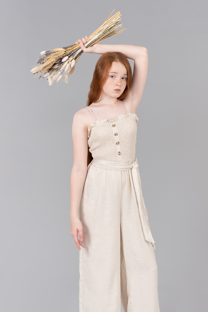 Teenage girl in beige overalls holding dried flowers