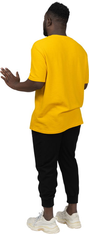 Three-quarter back view of a young dark-skinned man in yellow t-shirt outstretching his arms