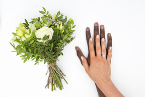 Female hand with a ring on the male hand and flower bouquet aside