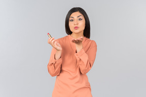 Indian woman in orange top holding lip balm and sending air kiss