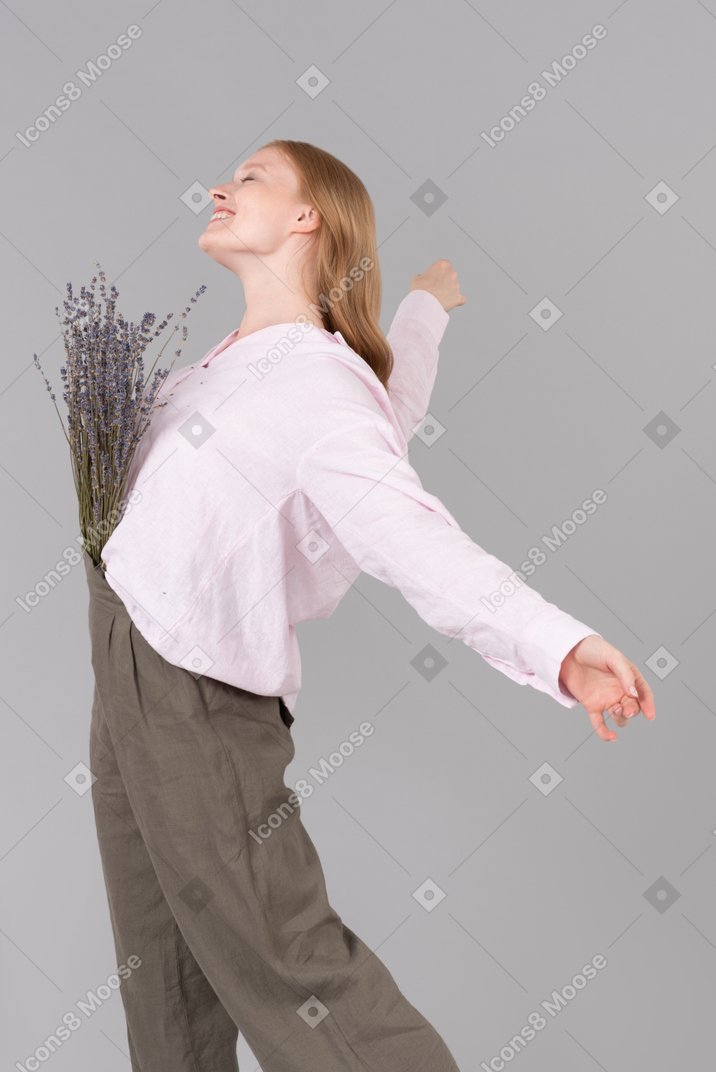 Smiling young woman standing with the flowers in her pants and arms open