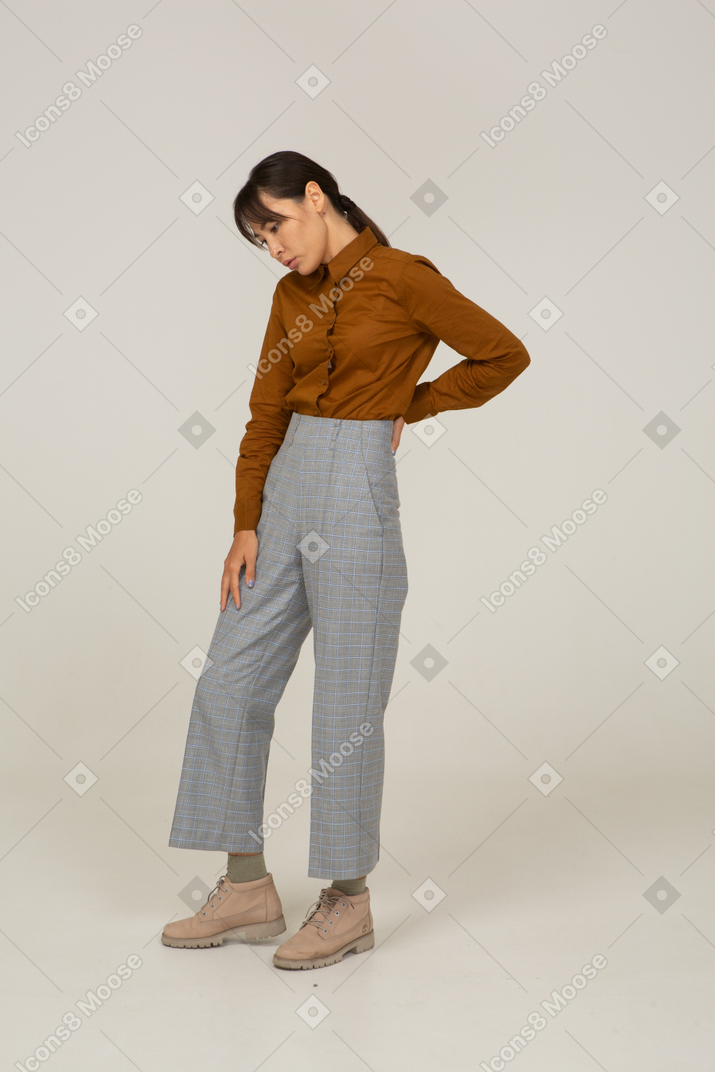 Vista de três quartos de uma jovem mulher asiática de calça e blusa tocando as costas